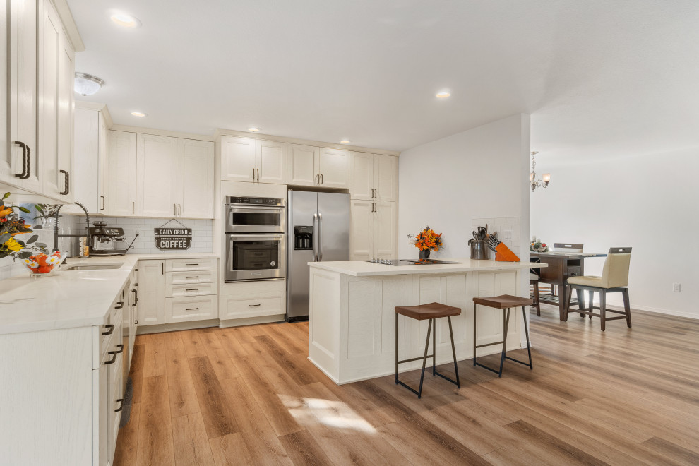 Mid-sized contemporary eat-in kitchen in Seattle with a double-bowl sink, shaker cabinets, white cabinets, quartz benchtops, white splashback, porcelain splashback, stainless steel appliances, laminate floors, a peninsula, brown floor and white benchtop.
