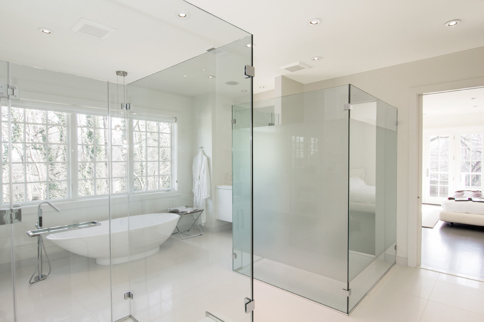 Inspiration for a large modern master bathroom in DC Metro with flat-panel cabinets, white cabinets, a freestanding tub, white tile, white walls, an undermount sink, solid surface benchtops, a curbless shower, a two-piece toilet, stone tile, cement tiles, white floor and a hinged shower door.