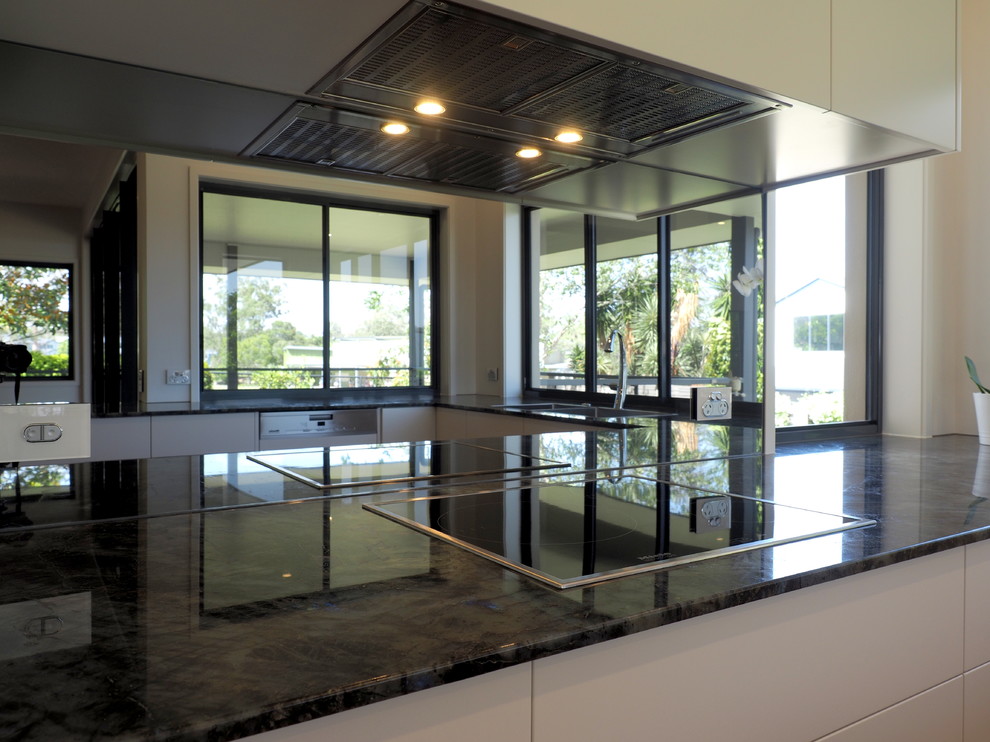 This is an example of a large contemporary u-shaped open plan kitchen in Brisbane with an undermount sink, flat-panel cabinets, white cabinets, granite benchtops, mirror splashback, stainless steel appliances, light hardwood floors, with island and multi-coloured benchtop.
