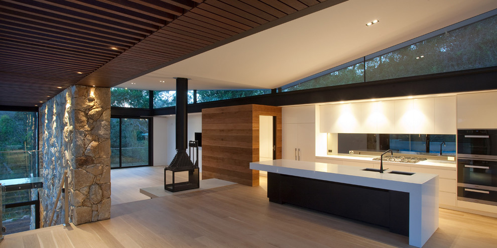 Mid-sized contemporary kitchen/dining combo in Melbourne with white walls, medium hardwood floors, a two-sided fireplace and a stone fireplace surround.