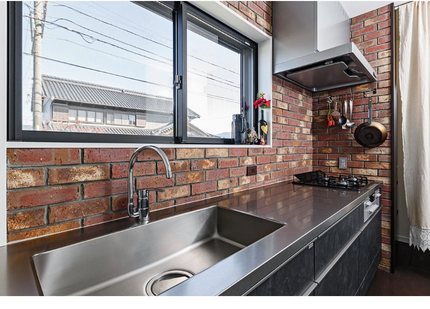 Foto på ett stort industriellt linjärt kök med öppen planlösning, med en integrerad diskho, svarta skåp, bänkskiva i rostfritt stål, rött stänkskydd, stänkskydd i tegel, rostfria vitvaror, plywoodgolv och brunt golv