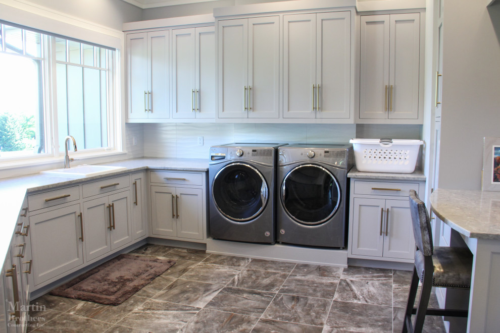 Dedicated laundry room - large transitional u-shaped porcelain tile dedicated laundry room idea in Other with a drop-in sink, shaker cabinets, gray cabinets, quartz countertops, white backsplash, ceramic backsplash, gray walls and a side-by-side washer/dryer