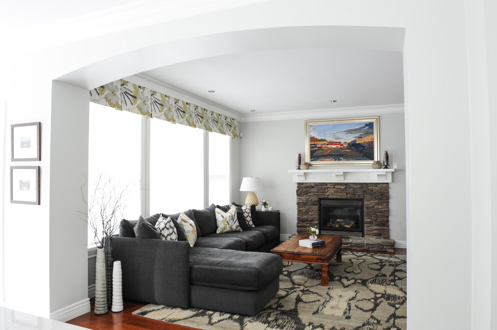 This is an example of a mid-sized transitional open concept family room in Vancouver with white walls, medium hardwood floors, a standard fireplace, a stone fireplace surround and a wall-mounted tv.