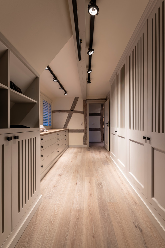 This is an example of a large country women's walk-in wardrobe in Frankfurt with grey cabinets, painted wood floors, grey floor and beaded inset cabinets.