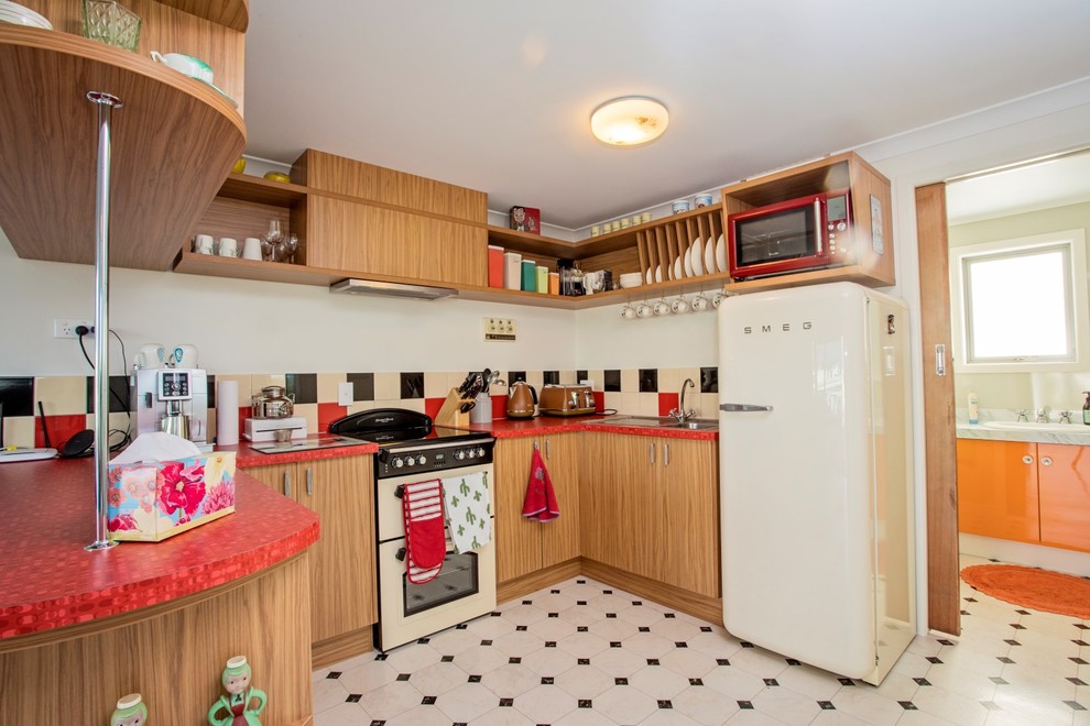 Photo of a mid-sized beach style u-shaped eat-in kitchen in Other with medium wood cabinets, multi-coloured splashback, ceramic splashback, coloured appliances, linoleum floors, white floor and red benchtop.