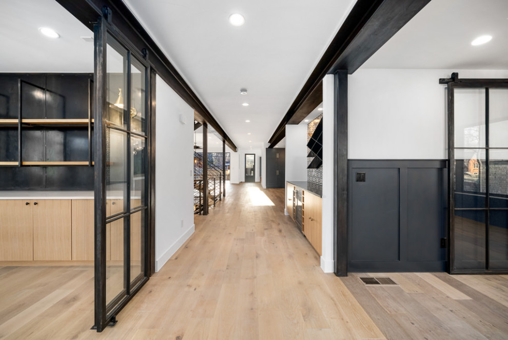 Inspiration for a large industrial hallway in Denver with white walls, light hardwood flooring, a single front door, a black front door, brown floors, exposed beams and wainscoting.