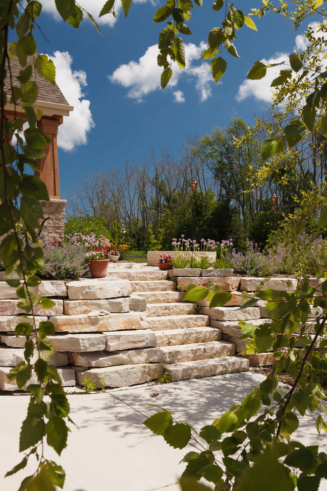 Large arts and crafts backyard full sun xeriscape in Milwaukee with a retaining wall and natural stone pavers for summer.
