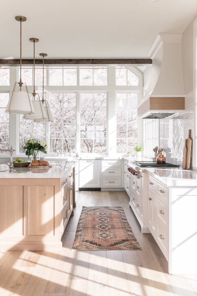 Inspiration for a mid-sized transitional u-shaped eat-in kitchen in Salt Lake City with a farmhouse sink, shaker cabinets, white cabinets, quartzite benchtops, white splashback, subway tile splashback, panelled appliances, light hardwood floors, with island, white benchtop and exposed beam.
