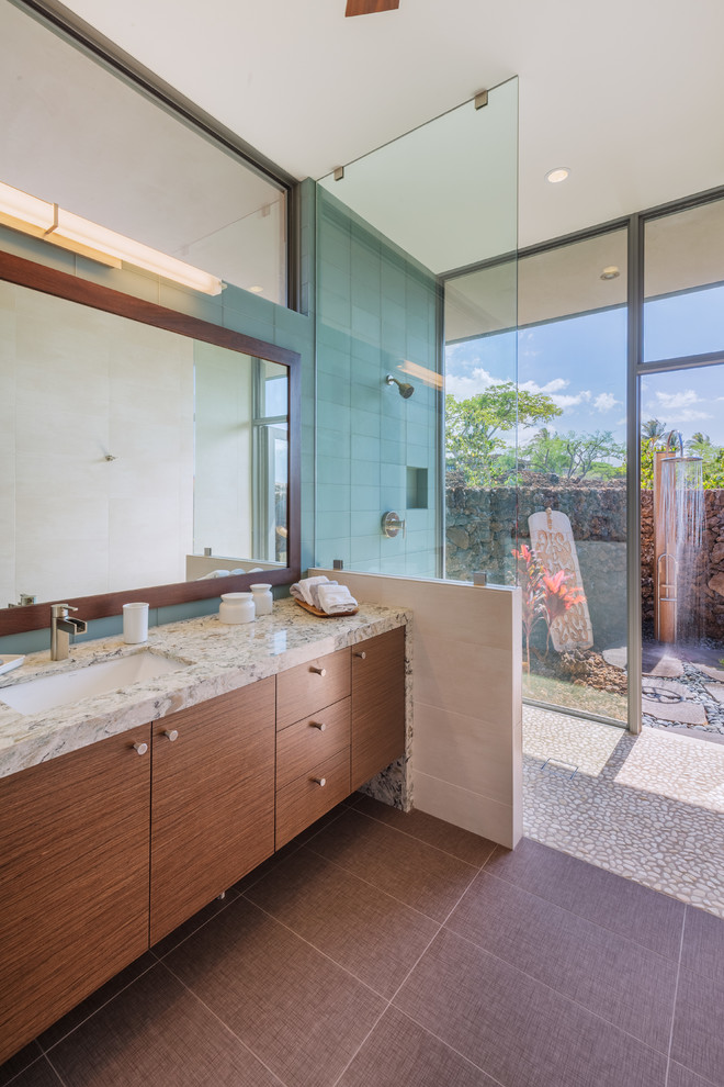 This is an example of a mid-sized contemporary master bathroom in Hawaii with flat-panel cabinets, dark wood cabinets, blue tile, glass tile, an undermount sink, an open shower, blue walls, pebble tile floors, granite benchtops, beige floor and an open shower.