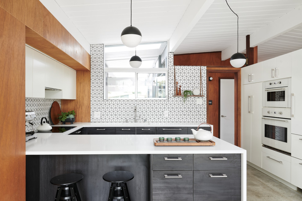 Midcentury u-shaped kitchen in San Francisco with an undermount sink, flat-panel cabinets, grey cabinets, white splashback, mosaic tile splashback, white appliances, concrete floors, a peninsula, grey floor, white benchtop, timber and vaulted.