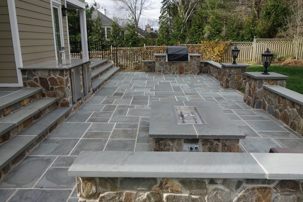 This is an example of a large traditional backyard patio in New York with an outdoor kitchen, natural stone pavers and no cover.
