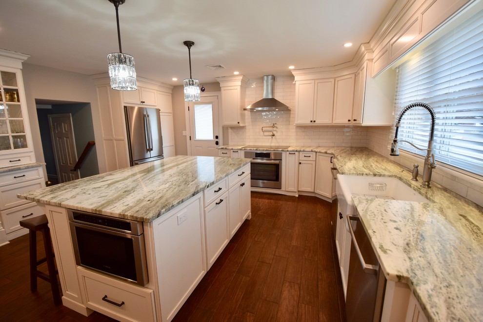 Large transitional u-shaped dark wood floor and brown floor enclosed kitchen photo with a farmhouse sink, beaded inset cabinets, white cabinets, granite countertops, beige backsplash, ceramic backsplash, stainless steel appliances, an island and multicolored countertops