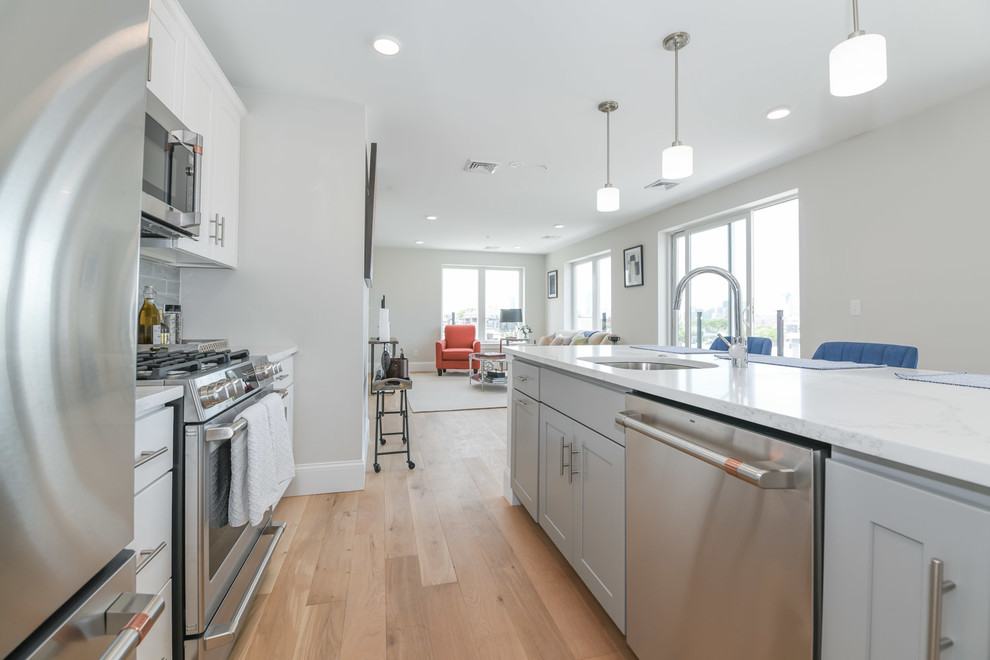 Eat-in kitchen - mid-sized transitional l-shaped medium tone wood floor and yellow floor eat-in kitchen idea in Boston with an undermount sink, shaker cabinets, white cabinets, quartz countertops, gray backsplash, ceramic backsplash, stainless steel appliances, an island and white countertops