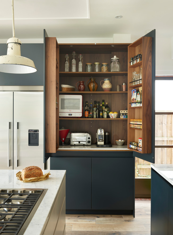 Photo of a large contemporary l-shaped eat-in kitchen in London with an integrated sink, blue cabinets, marble benchtops, metallic splashback, mirror splashback, light hardwood floors, with island, brown floor and white benchtop.