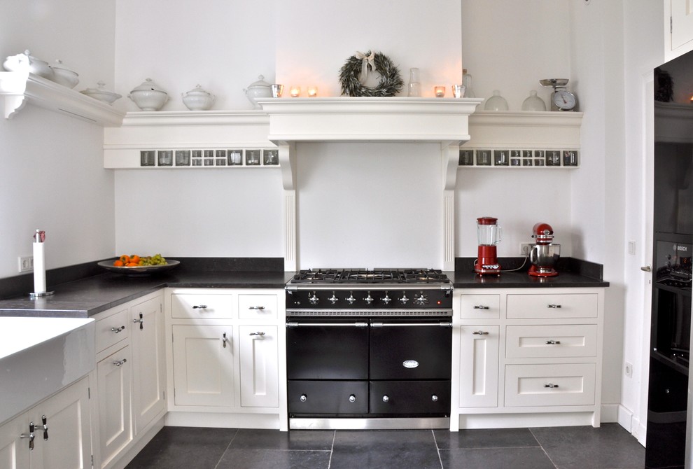 Photo of a traditional separate kitchen in Berlin with a farmhouse sink, recessed-panel cabinets, white cabinets, white splashback, black appliances and no island.