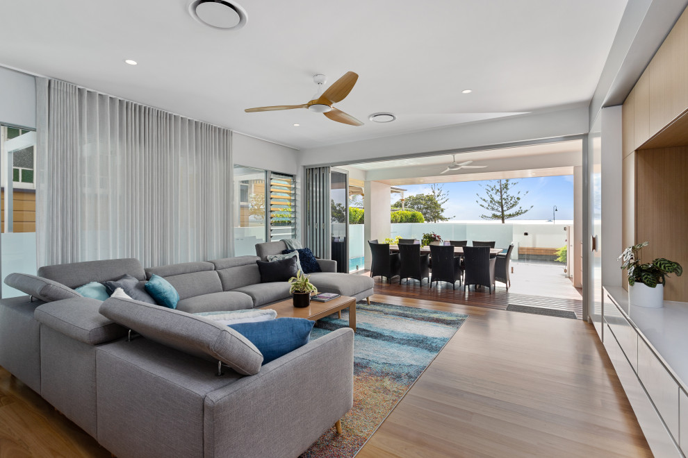 Large beach style open concept living room in Brisbane with white walls, medium hardwood floors, a built-in media wall, brown floor and exposed beam.