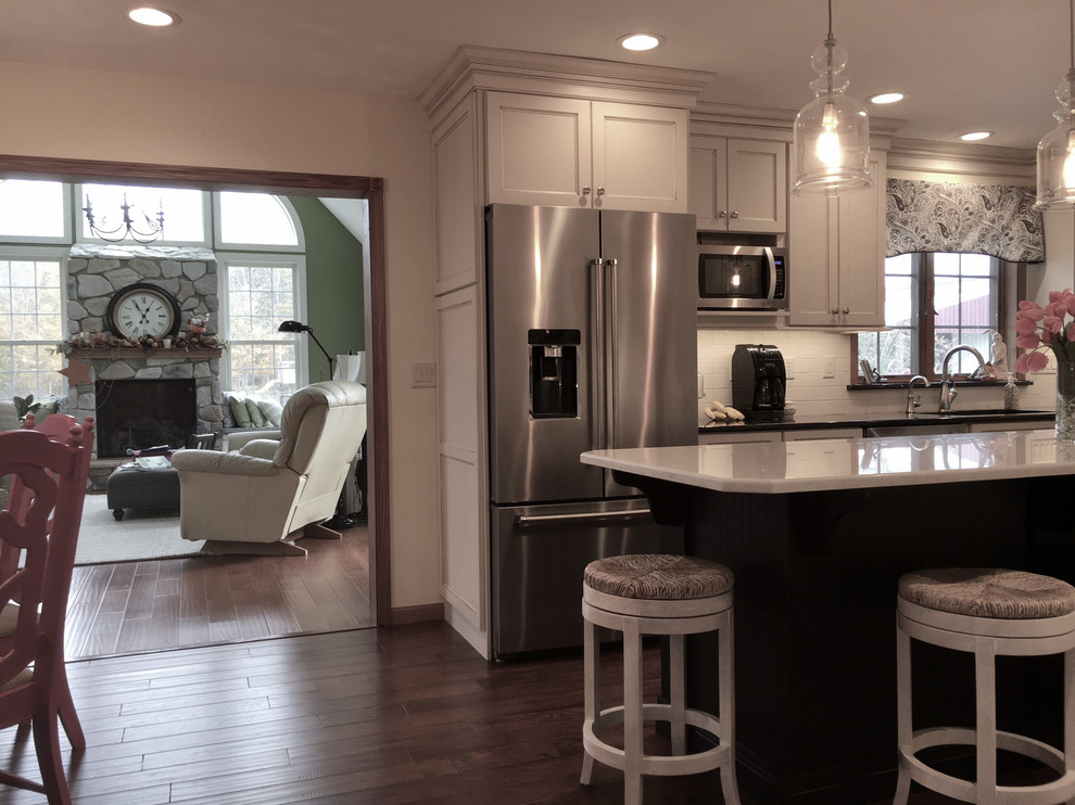 Example of a large transitional medium tone wood floor and brown floor eat-in kitchen design with an undermount sink, flat-panel cabinets, white cabinets, granite countertops, white backsplash, porcelain backsplash, stainless steel appliances and an island