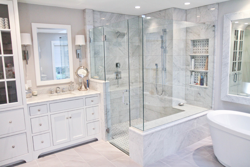 Photo of a large traditional master bathroom in Philadelphia with an undermount sink, white cabinets, marble benchtops, a freestanding tub, a corner shower, a one-piece toilet, gray tile, stone tile, grey walls, porcelain floors and recessed-panel cabinets.