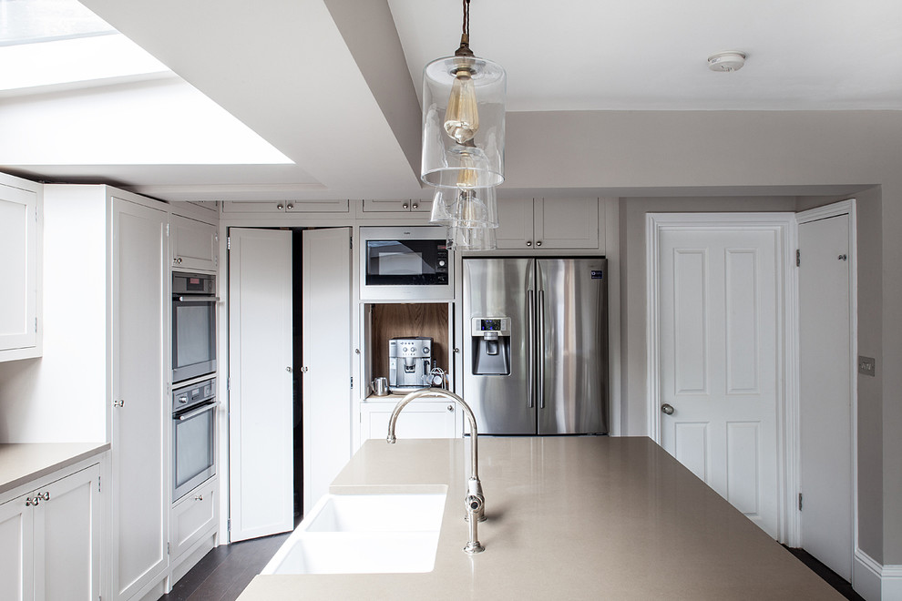 Large transitional u-shaped eat-in kitchen in London with a farmhouse sink, shaker cabinets, beige cabinets, granite benchtops, white splashback, subway tile splashback, stainless steel appliances, dark hardwood floors and with island.