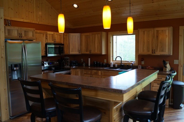 Mid-sized mountain style single-wall medium tone wood floor and beige floor open concept kitchen photo with a double-bowl sink, raised-panel cabinets, red cabinets, granite countertops, gray backsplash, stone tile backsplash, stainless steel appliances and an island