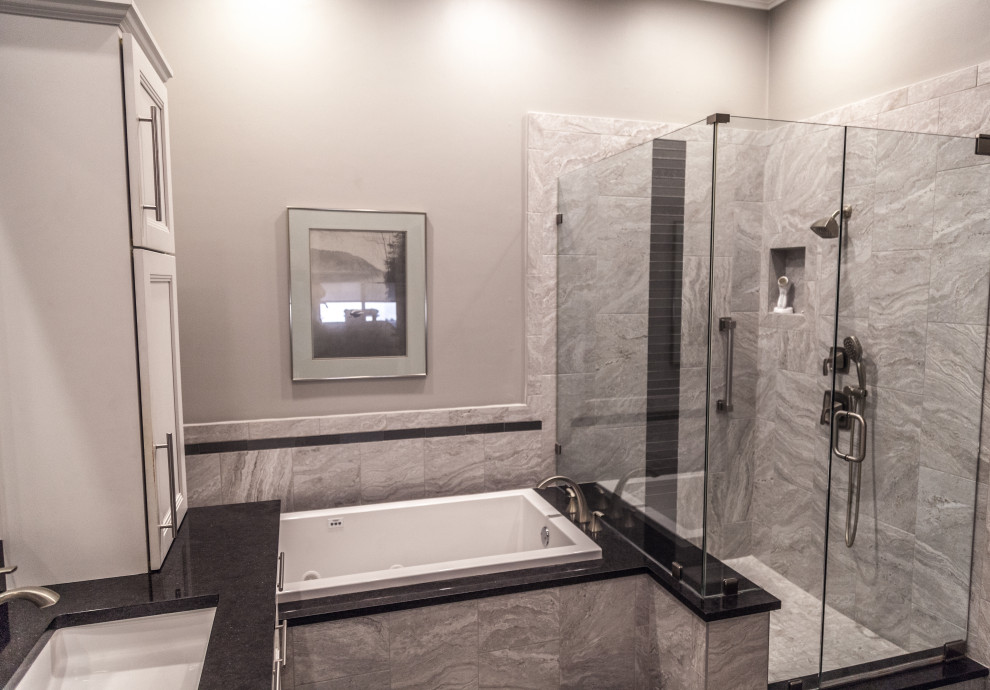Example of a transitional master gray tile and ceramic tile marble floor, gray floor and double-sink drop-in bathtub design with a two-piece toilet, gray walls, an undermount sink, quartzite countertops, a hinged shower door, black countertops and a niche