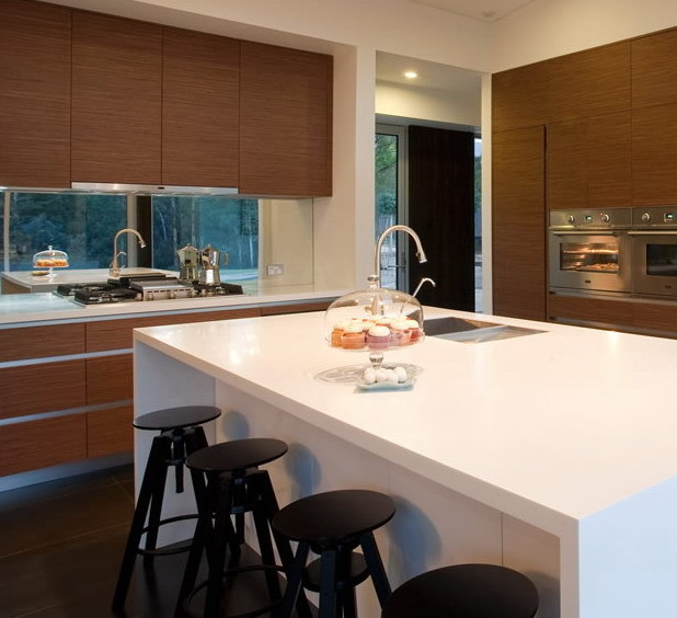 Inspiration for an expansive contemporary l-shaped eat-in kitchen in Melbourne with an undermount sink, flat-panel cabinets, medium wood cabinets, solid surface benchtops, mirror splashback and stainless steel appliances.