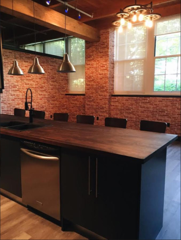 Photo of a mid-sized industrial galley open plan kitchen in Orange County with a double-bowl sink, flat-panel cabinets, black cabinets, wood benchtops, black splashback, subway tile splashback, stainless steel appliances, painted wood floors and with island.