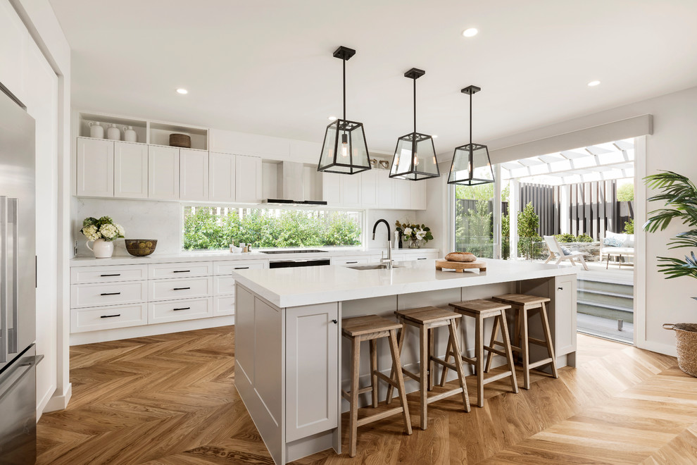 This is an example of a large transitional galley eat-in kitchen in Melbourne with an undermount sink, shaker cabinets, white cabinets, quartz benchtops, white splashback, stone slab splashback, black appliances, light hardwood floors, with island, brown floor and white benchtop.