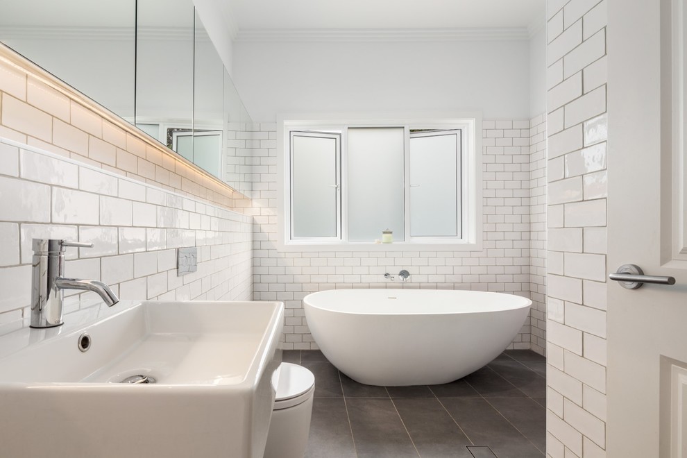 Design ideas for a mid-sized eclectic master bathroom in Sydney with recessed-panel cabinets, a freestanding tub, an alcove shower, a wall-mount toilet, white tile, ceramic tile, white walls, ceramic floors and a wall-mount sink.