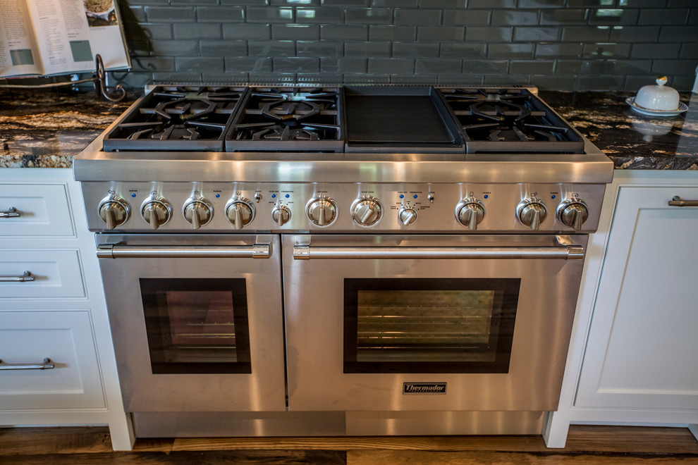 Example of a large transitional medium tone wood floor eat-in kitchen design in Atlanta with an undermount sink, recessed-panel cabinets, white cabinets, granite countertops, black backsplash, glass tile backsplash, stainless steel appliances and an island