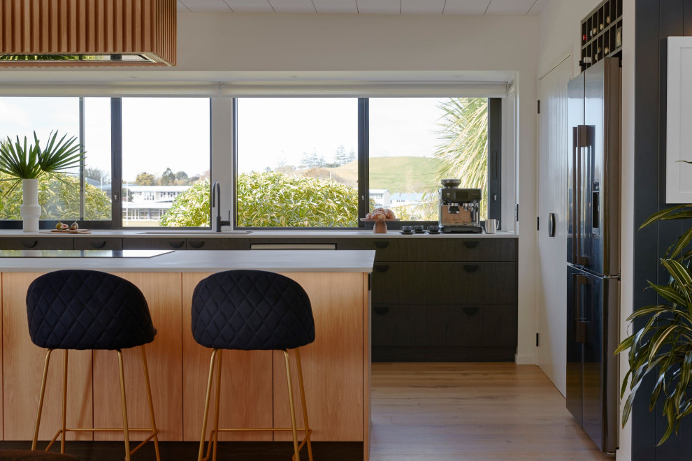 Modern galley kitchen in Auckland with a submerged sink, black appliances, an island and grey worktops.