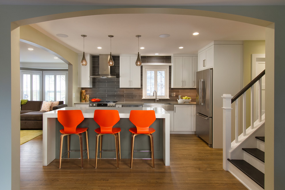 Example of a mid-sized transitional single-wall medium tone wood floor eat-in kitchen design in Minneapolis with a farmhouse sink, shaker cabinets, white cabinets, quartz countertops, gray backsplash, cement tile backsplash, stainless steel appliances and an island
