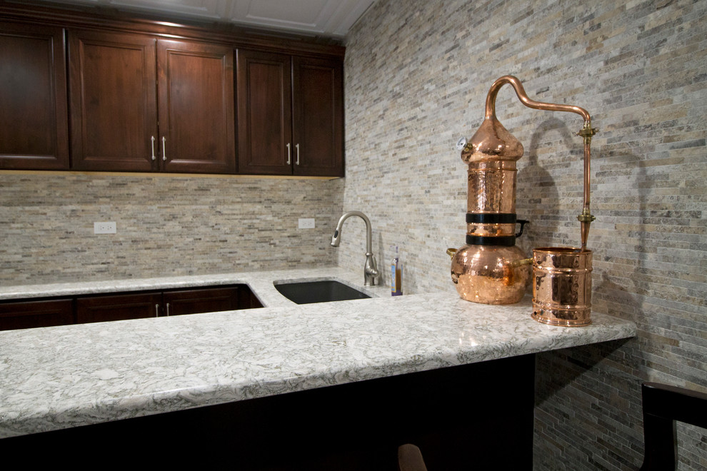 This is an example of a large traditional galley wet bar in Chicago with an undermount sink, recessed-panel cabinets, dark wood cabinets, quartz benchtops, grey splashback, travertine splashback, laminate floors and grey floor.