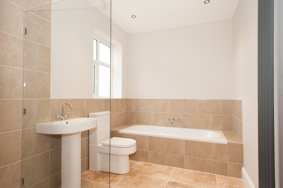 This is an example of a mid-sized contemporary kids bathroom in Other with a drop-in tub, a curbless shower, a two-piece toilet, beige tile, stone tile, grey walls, travertine floors and a pedestal sink.