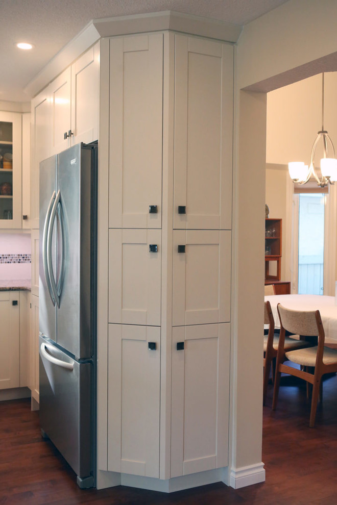 Inspiration for a mid-sized transitional l-shaped medium tone wood floor and brown floor open concept kitchen remodel in Calgary with an undermount sink, shaker cabinets, white cabinets, granite countertops, white backsplash, mosaic tile backsplash, stainless steel appliances, an island and beige countertops
