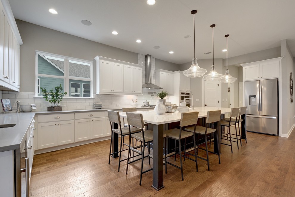 Design ideas for a transitional u-shaped kitchen in Jacksonville with an undermount sink, shaker cabinets, white cabinets, white splashback, subway tile splashback, stainless steel appliances, medium hardwood floors, with island, brown floor and multi-coloured benchtop.