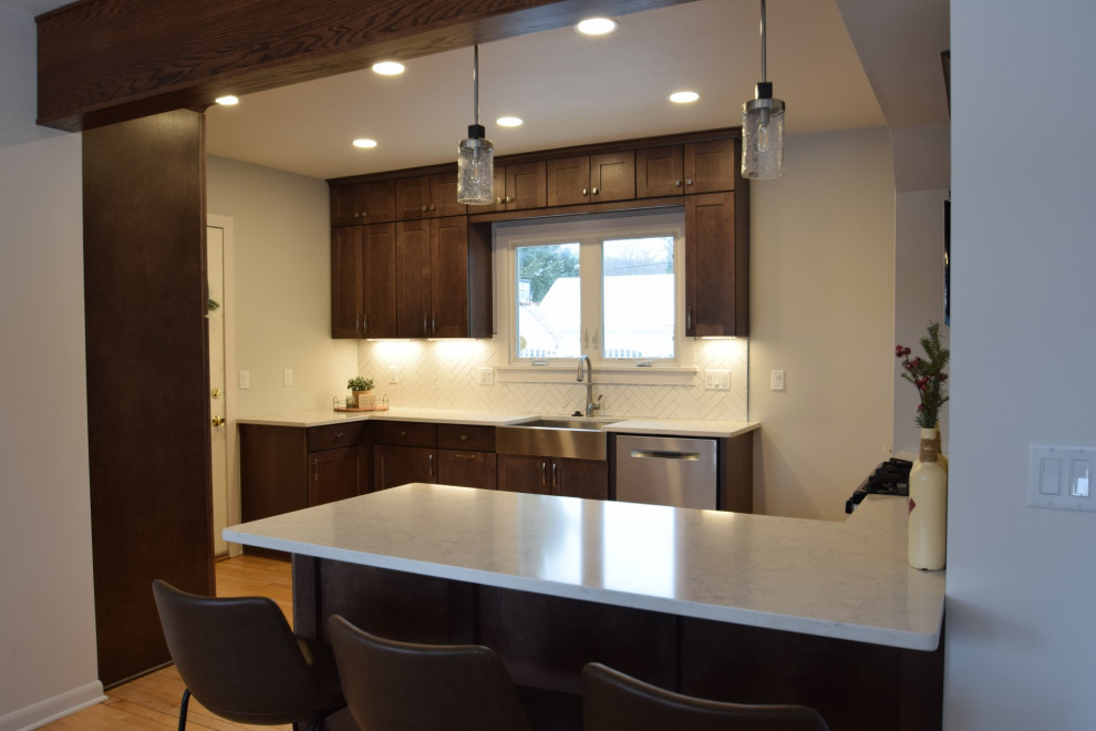 Inspiration for a transitional light wood floor eat-in kitchen remodel with a farmhouse sink, shaker cabinets, medium tone wood cabinets, quartz countertops, white backsplash, ceramic backsplash, stainless steel appliances and a peninsula
