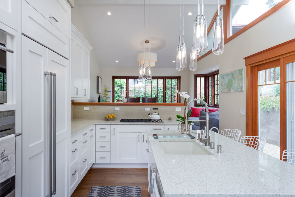 Mid-sized transitional l-shaped eat-in kitchen in San Francisco with an undermount sink, shaker cabinets, white cabinets, recycled glass benchtops, glass tile splashback, medium hardwood floors, with island, beige splashback and panelled appliances.