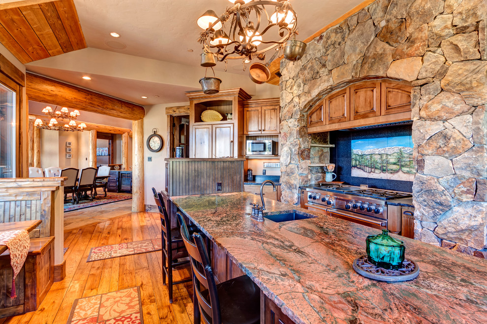 Example of a large mountain style u-shaped medium tone wood floor and brown floor eat-in kitchen design with louvered cabinets, distressed cabinets, granite countertops, beige backsplash, stone tile backsplash, stainless steel appliances, an island and red countertops