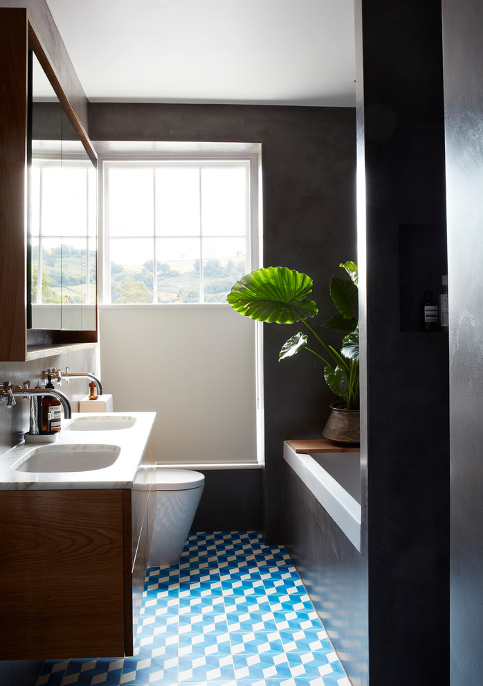 Inspiration for a mid-sized contemporary kids wet room bathroom in Devon with flat-panel cabinets, medium wood cabinets, a drop-in tub, gray tile, cement tile, cement tiles, marble benchtops, blue floor, an open shower, white benchtops, black walls and an undermount sink.