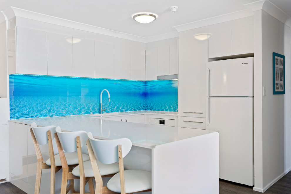 Inspiration for a small beach style u-shaped eat-in kitchen in Gold Coast - Tweed with an undermount sink, flat-panel cabinets, white cabinets, quartz benchtops, blue splashback, glass sheet splashback, white appliances and white benchtop.