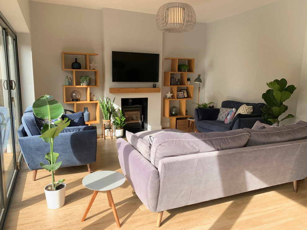 Photo of a large scandinavian open concept living room in Hertfordshire with a library, grey walls, laminate floors, a wood stove, a plaster fireplace surround and a wall-mounted tv.
