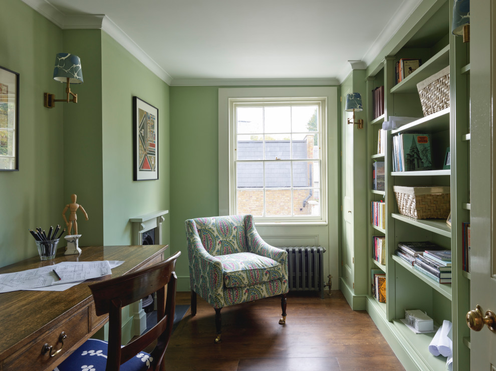 Design ideas for a mid-sized traditional home office in London with a library, green walls, dark hardwood floors, a standard fireplace, a stone fireplace surround, a freestanding desk and brown floor.
