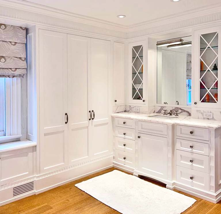 Design ideas for a mid-sized traditional master bathroom in New York with shaker cabinets, white cabinets, a japanese tub, an open shower, a one-piece toilet, white tile, white walls, medium hardwood floors, a drop-in sink, engineered quartz benchtops, brown floor, a sliding shower screen, white benchtops, an enclosed toilet, a double vanity, a built-in vanity, coffered and wood walls.