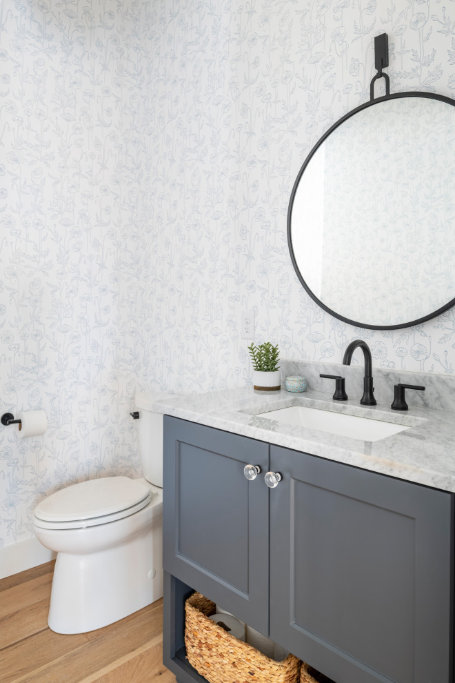 Transitional powder room in Minneapolis with shaker cabinets, grey cabinets, a two-piece toilet, multi-coloured walls, medium hardwood floors, an undermount sink, marble benchtops, brown floor, grey benchtops, a built-in vanity and wallpaper.