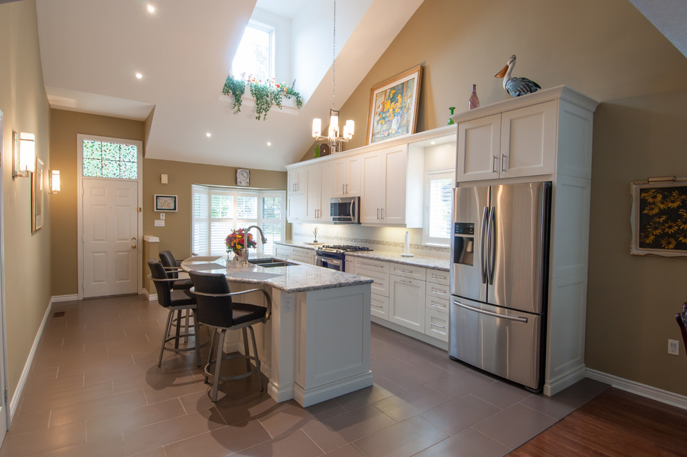 Example of a mid-sized transitional galley ceramic tile eat-in kitchen design in Toronto with a double-bowl sink, shaker cabinets, white cabinets, beige backsplash, stone tile backsplash, stainless steel appliances, an island and granite countertops