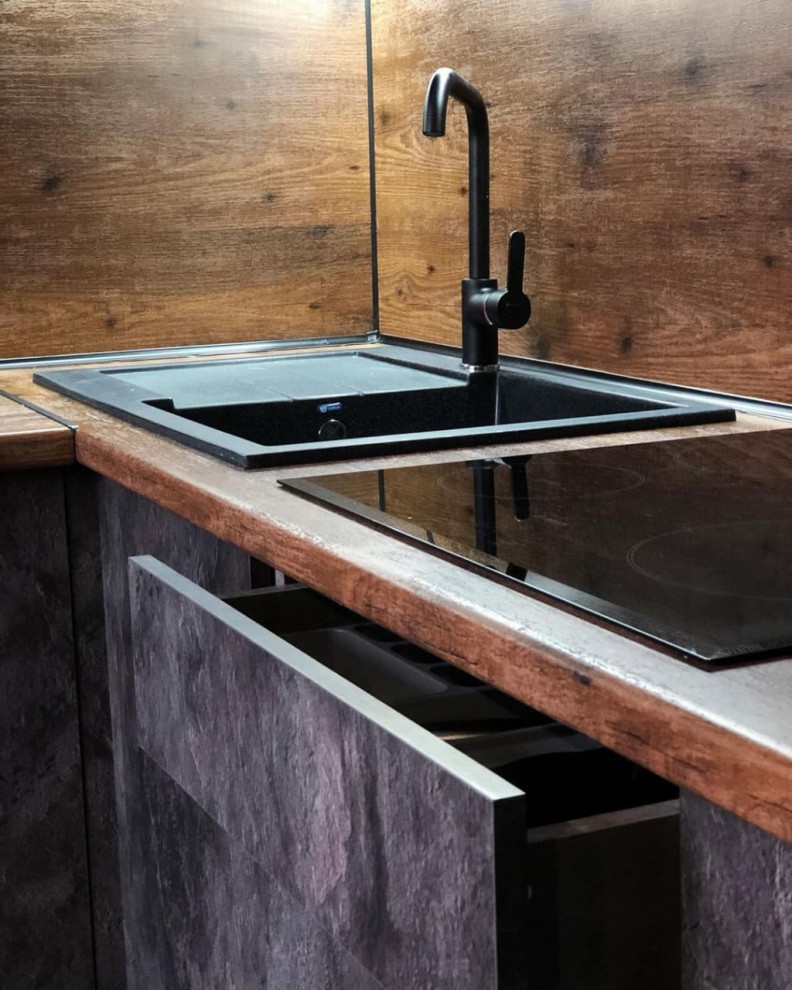 This is an example of a small industrial l-shaped eat-in kitchen in Moscow with a drop-in sink, raised-panel cabinets, black cabinets, wood benchtops, brown splashback, timber splashback, black appliances, linoleum floors, no island, brown floor and brown benchtop.