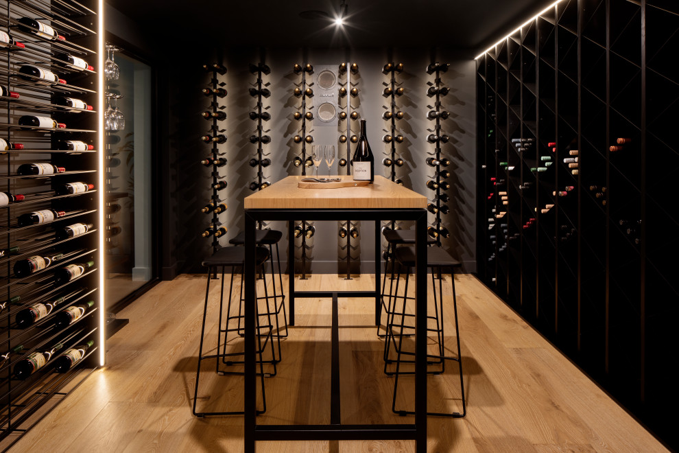 Cette image montre une grande cave à vin design avec parquet clair, des casiers et un sol marron.