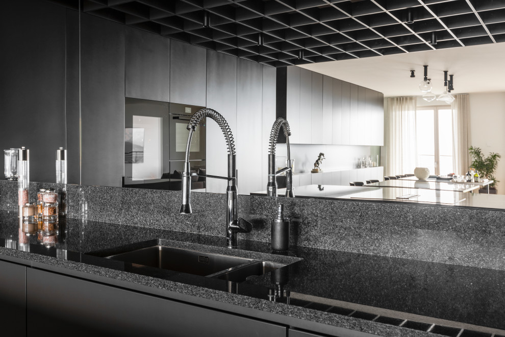 Inspiration for a modern u-shaped open plan kitchen in Milan with a built-in sink, flat-panel cabinets, grey cabinets, granite worktops, black splashback, granite splashback, black appliances, light hardwood flooring, an island and black worktops.