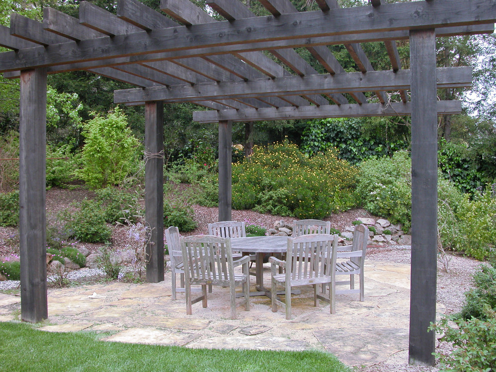 This is an example of a traditional backyard patio in Other with a pergola and natural stone pavers.